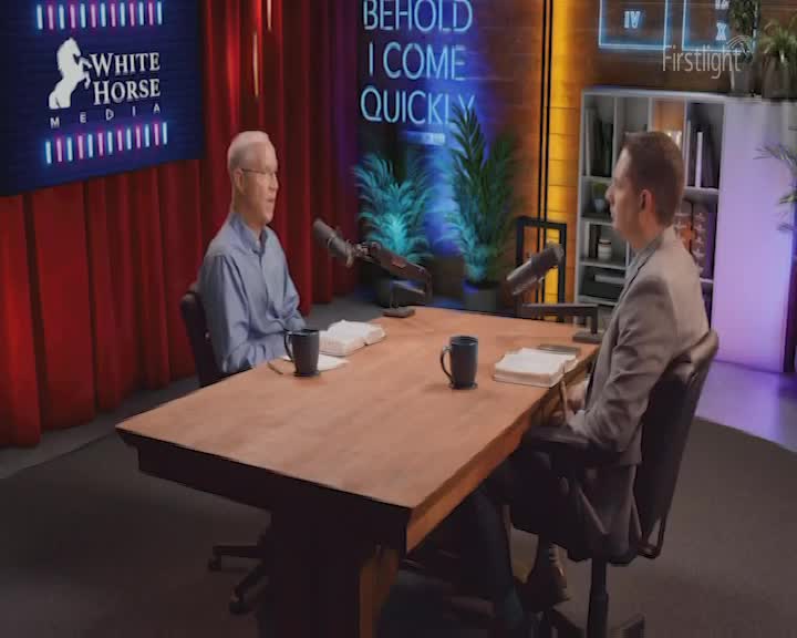 Two men sit across from each other at a large wooden table, microphones between them. A blue neon sign behind them reads "BEHOLD I COME QUICKLY."