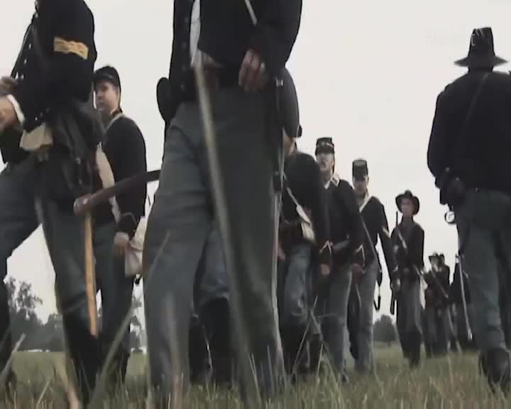 The soldiers march forward in their dark uniforms, their rifles held ready. The sky above is a pale, overcast grey.