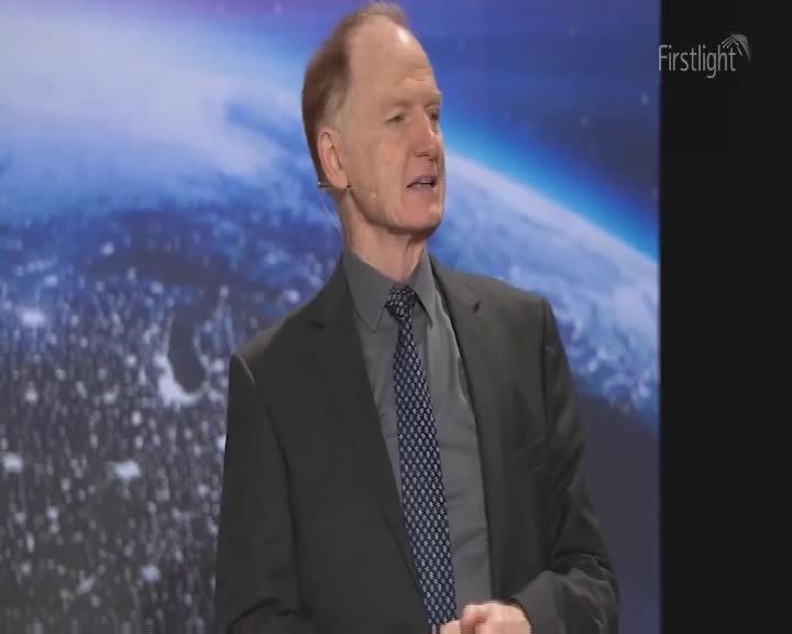A man in a suit stands before a large screen displaying the Earth. The Firstlight logo appears in the corner.