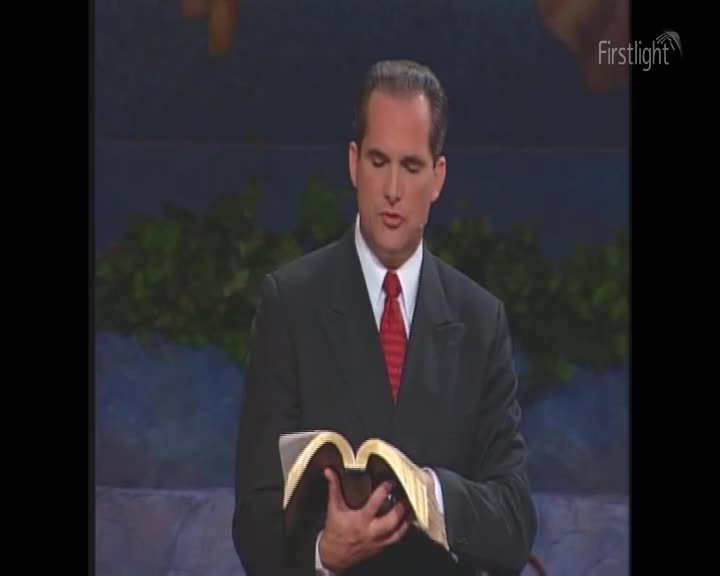 A man in a dark suit and red tie holds a thick book open, his gaze fixed on its pages. The early morning light catches the gold trim of the book as he prepares to speak.