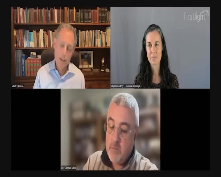 A man in a light blue shirt speaks, his bookshelf behind him. To his right, a woman with dark hair looks directly at the camera. Below them, a man with glasses and a grey beard is visible.