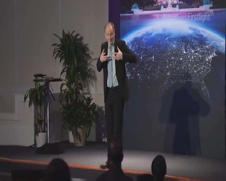 A man in a suit gestures emphatically on a stage, his hands spread wide. Behind him, a large screen displays a nighttime view of Earth, dotted with city lights, with "Firstlight" subtly overlaid. A man in a suit gestures emphatically on a stage, his hands spread wide. Behind him, a large screen displays a nighttime view of Earth, dotted with city lights, with "Firstlight" subtly overlaid.