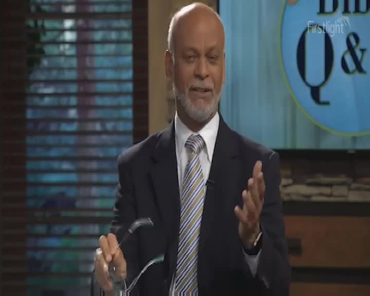 A man in a suit and tie speaks, gesturing with his hands. He holds a pair of glasses in his left hand, their frames catching the light. A man in a suit and tie speaks, gesturing with his hands. He holds a pair of glasses in his left hand, their frames catching the light.