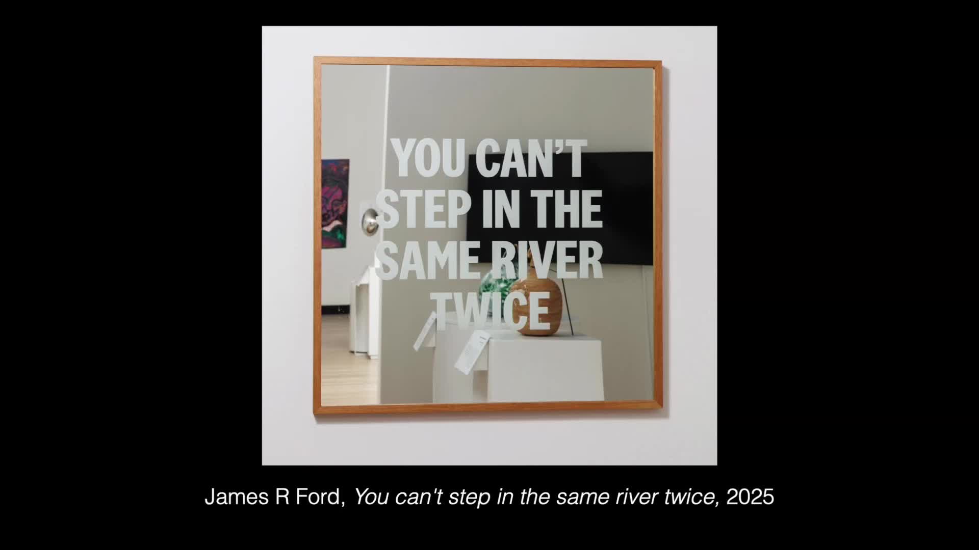 A large mirror hangs on a white wall, reflecting the words "YOU CAN'T STEP IN THE SAME RIVER TWICE" in white lettering. In the reflection, a brown, gourd-like object sits on a white pedestal.