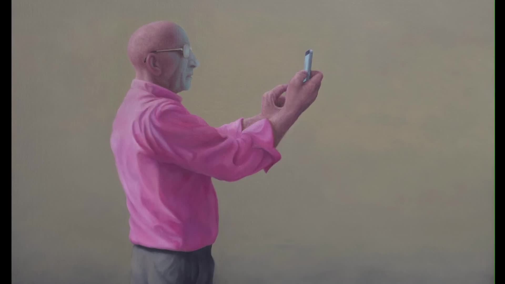 A man in a bright pink shirt holds his phone up, likely recording something for Parliament TV. His fingers are poised over the screen, as if he's about to press a button. A man in a bright pink shirt holds his phone up, likely recording something for Parliament TV. His fingers are poised over the screen, as if he's about to press a button.