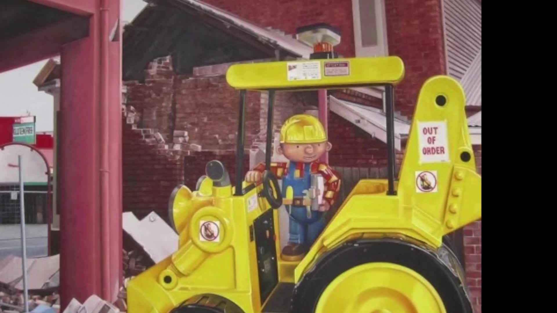 Bob the Builder sits in his yellow digger, a sign on the arm reading "OUT OF ORDER." The backdrop looks like a partially demolished brick building, a common sight after the Canterbury earthquakes.