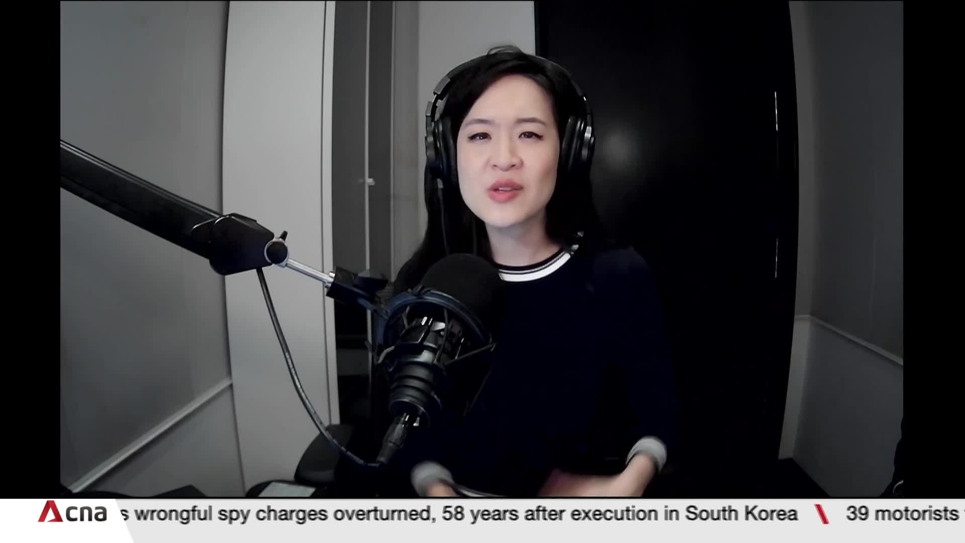 A woman with headphones speaks into a microphone, her face illuminated by the studio lights. The CNA International logo and breaking news crawl along the bottom of the screen.
