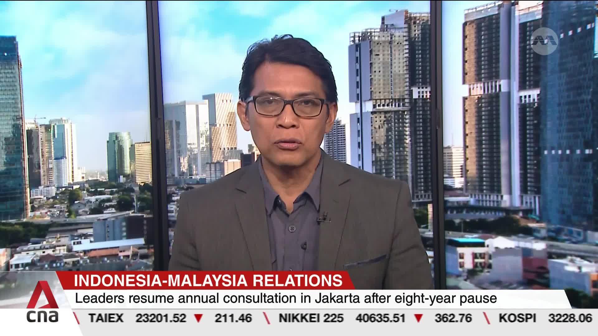 A man in glasses, wearing a blazer, is speaking directly to the camera. Behind him, a cityscape of tall buildings is visible through a large window, with the CNA logo displayed at the bottom.

