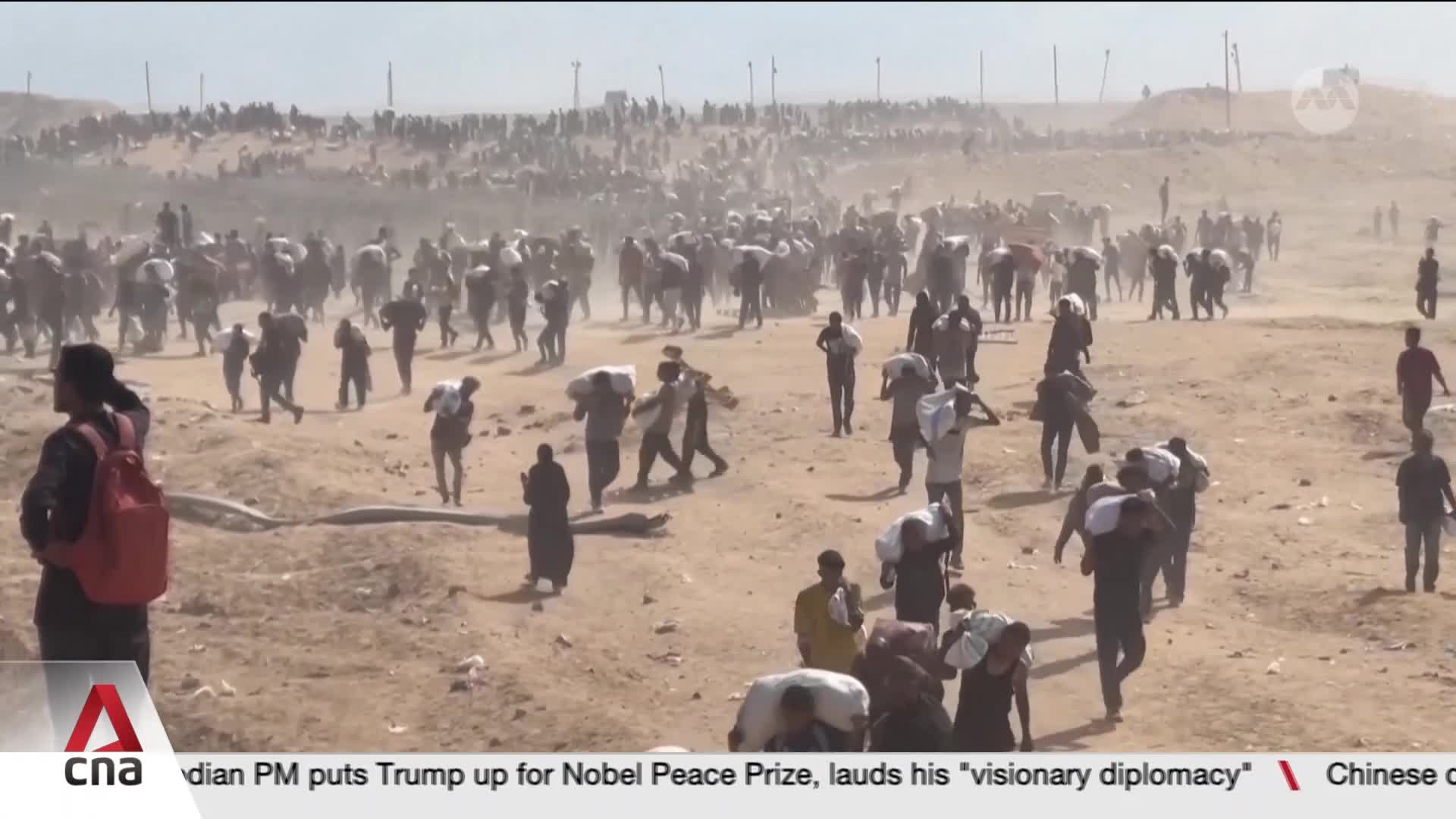 A mass of people, many carrying bundles over their shoulders, are moving across a dusty landscape. The air is thick with dust as they walk, a scene reported by CNA International.
