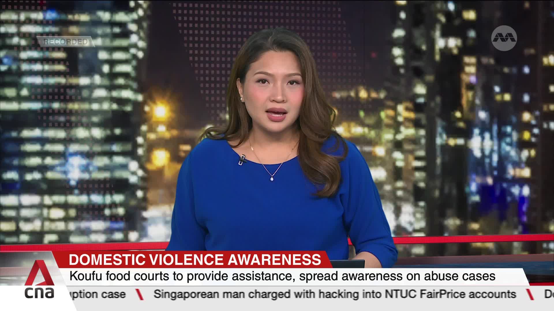A woman in a blue blouse is speaking directly to the camera, framed against a backdrop of city lights. The CNA International logo is visible, and a news banner about domestic violence awareness is displayed below.
