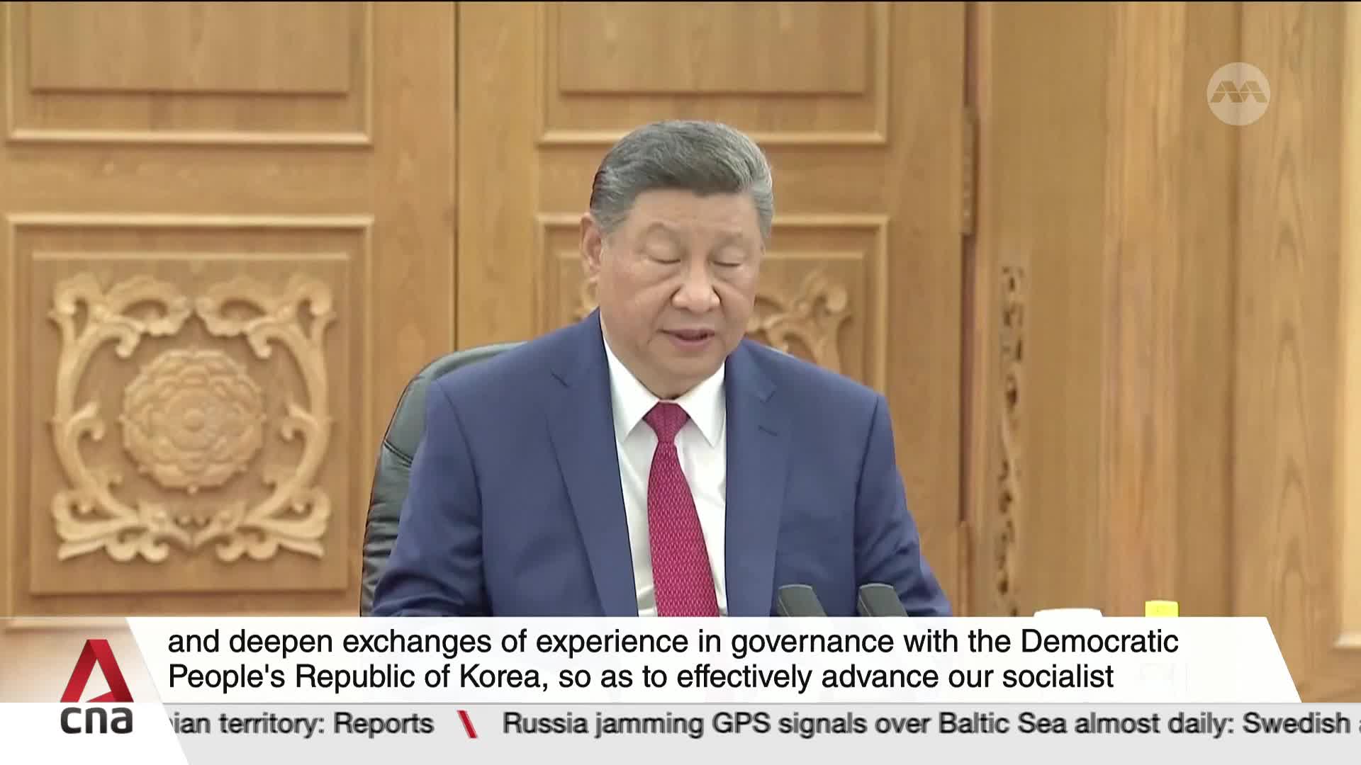 A man in a blue suit and red tie is speaking, his lips moving as he reads from a document. The CNA International logo is visible in the lower left corner, and text scrolls across the bottom of the screen.
