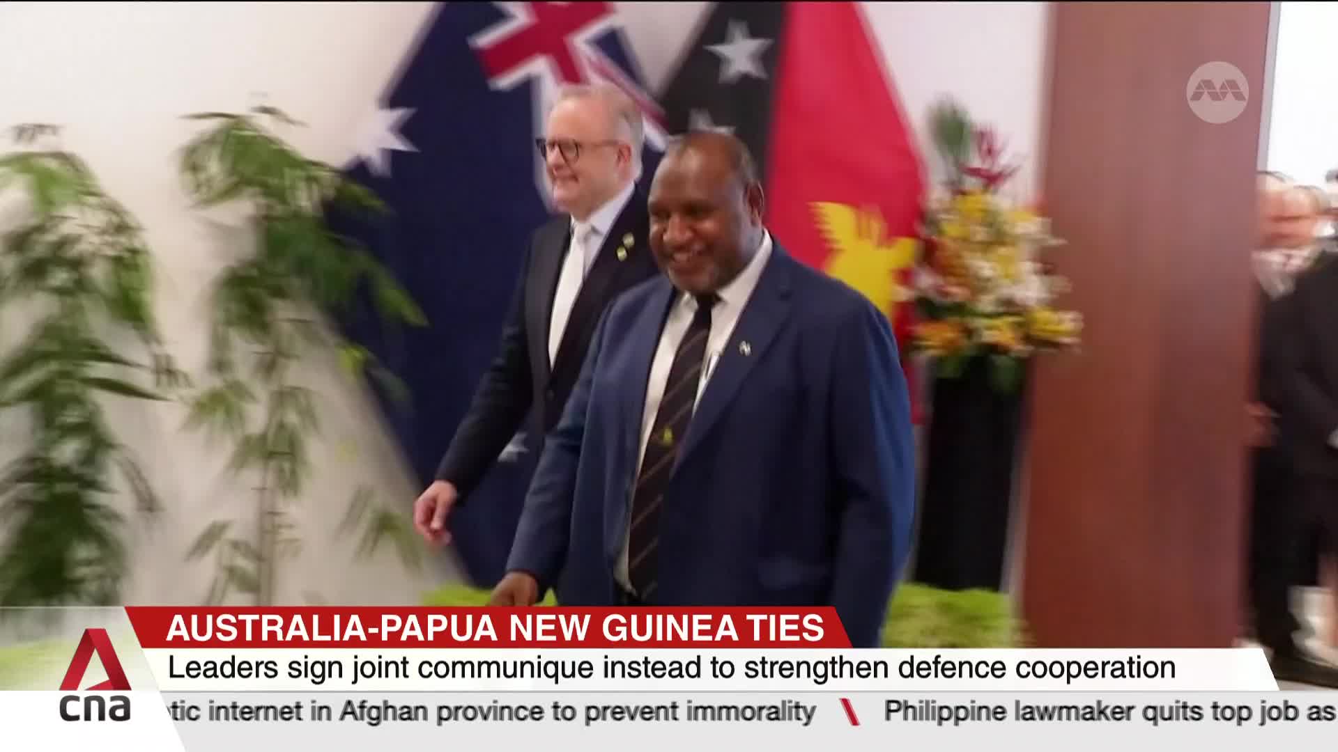 Two men in suits are walking towards the camera, smiling. Behind them, the flags of Australia and Papua New Guinea are visible, as reported by CNA International.
