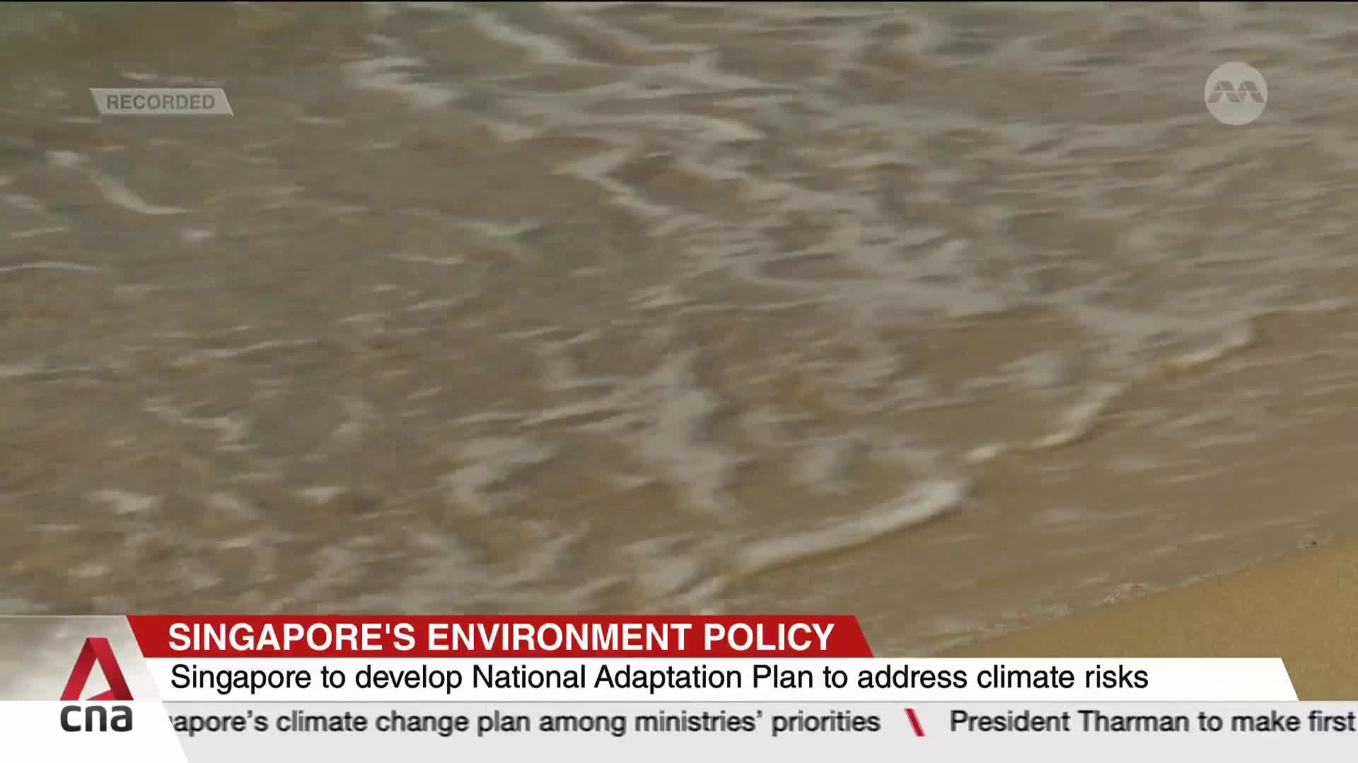 Gentle waves lap at the sandy shore, the water a mix of white foam and light brown. The CNA International graphic at the bottom highlights Singapore's climate change adaptation plan.

