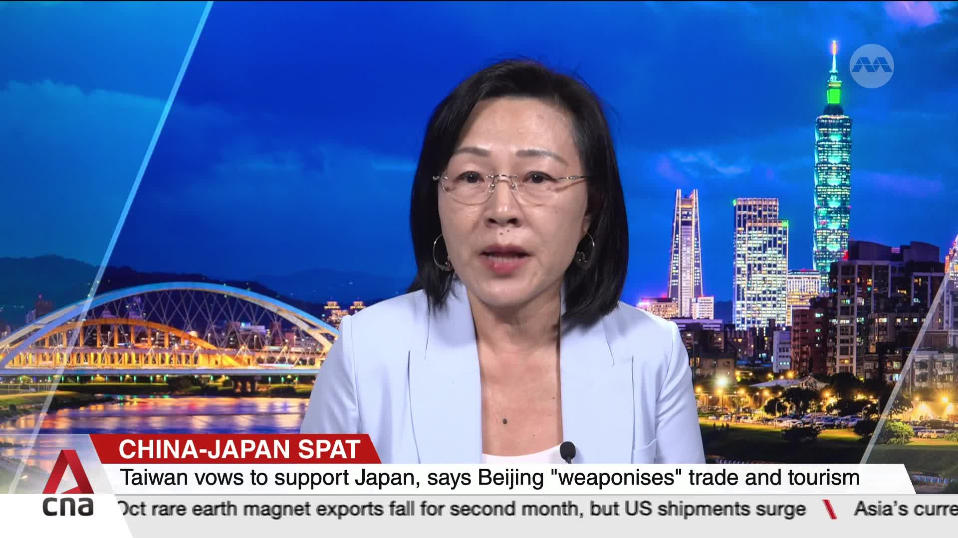 A woman in a light blue blazer speaks directly to the camera, framed by a backdrop of a city skyline at dusk. The CNA International logo is visible in the corner, with a headline about a China-Japan spat.
