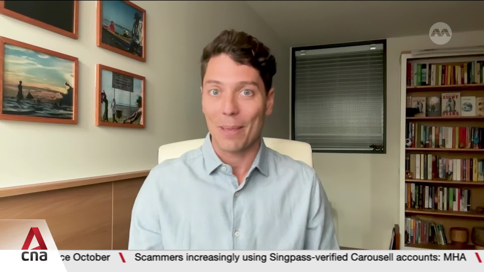 A man in a light blue shirt is speaking directly to the camera, his expression open and engaged. The CNA International logo is visible in the corner, and a news ticker scrolls across the bottom of the screen.

