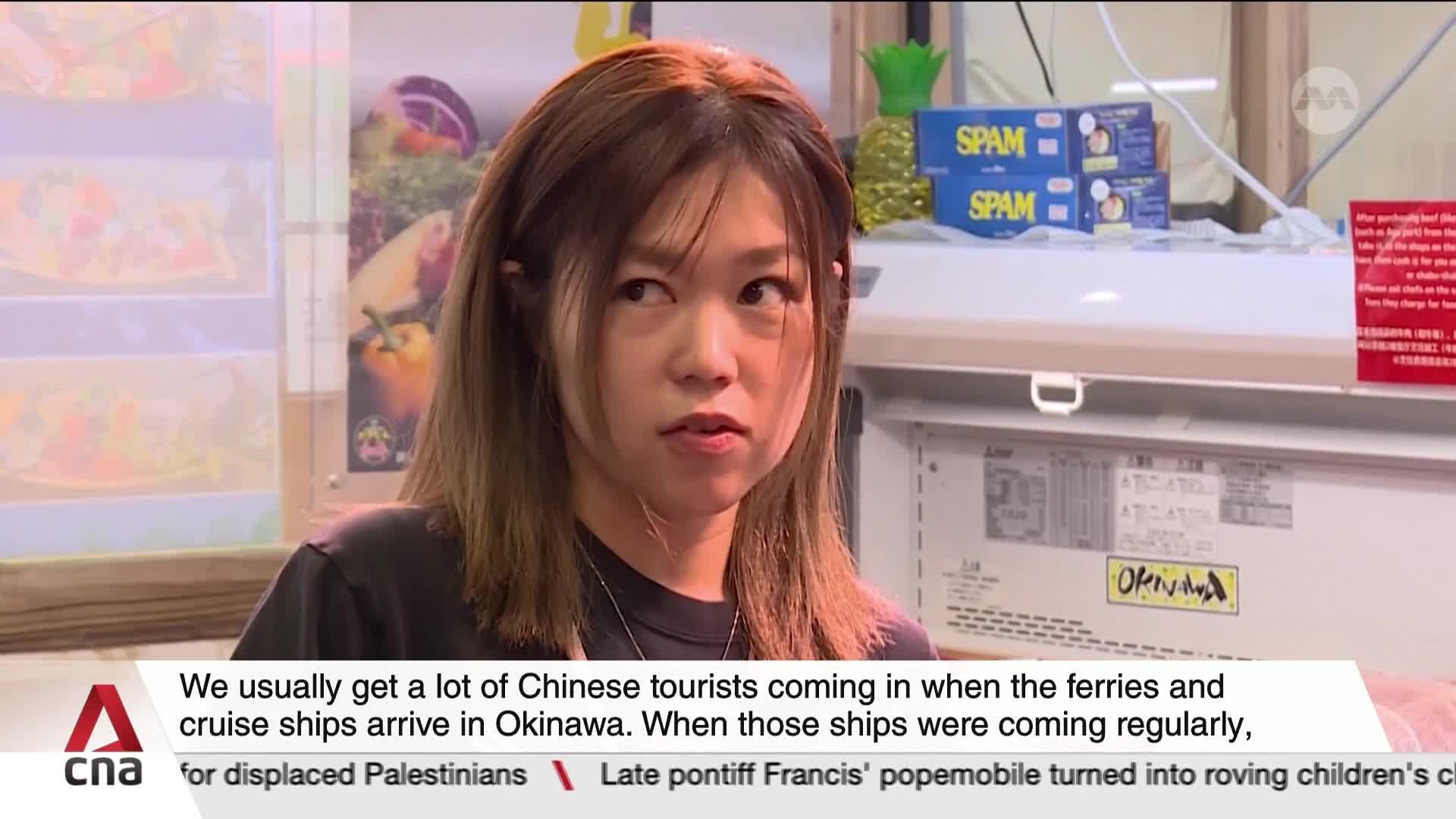 A woman with brown hair looks directly at the camera, speaking. Below her, a CNA International graphic displays a caption about Chinese tourists in Okinawa.
