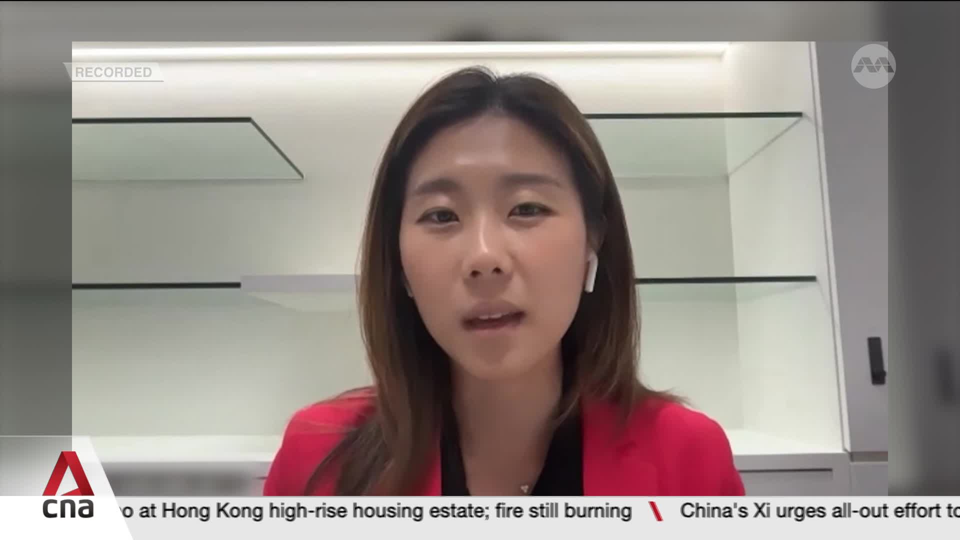 A woman in a red blazer speaks directly to the camera, wearing earbuds. Below, the CNA International logo and news headlines scroll across the bottom of the screen.
