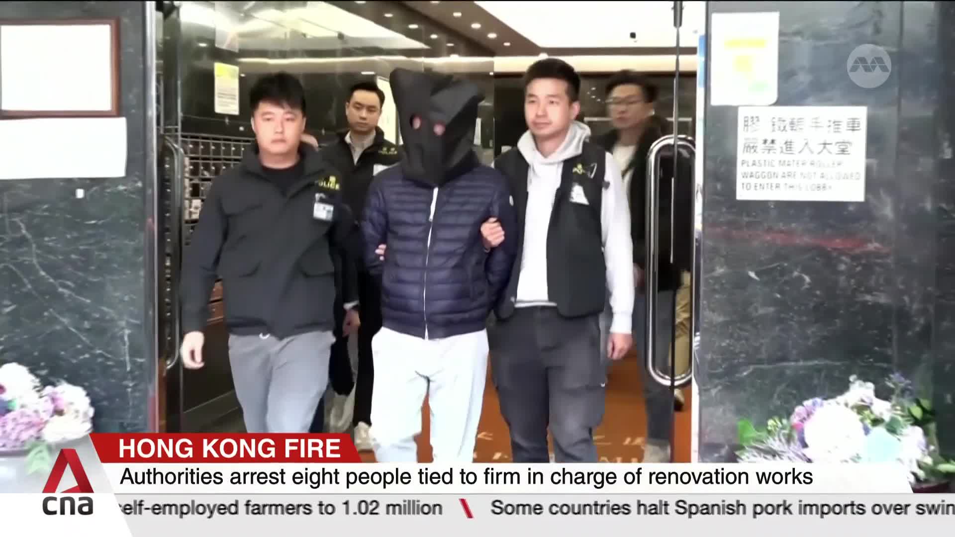 A man in a black hood is escorted by two others, all heading toward the camera. The CNA International graphic at the bottom of the screen identifies the story as a Hong Kong fire-related arrest.
