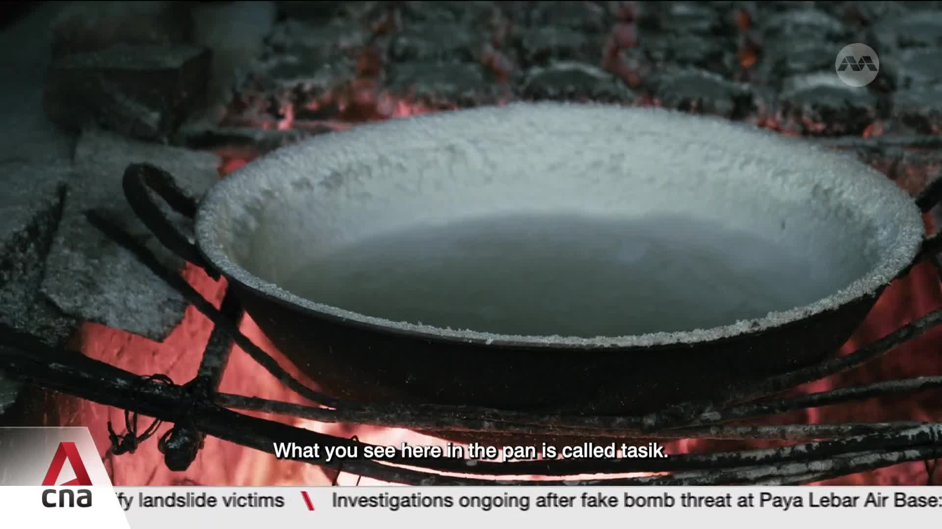 A white, powdery substance coats the rim of a dark pan, which sits over glowing red embers. This is tasik, a traditional ingredient being prepared. A white, powdery substance coats the rim of a dark pan, which sits over glowing red embers. This is tasik, a traditional ingredient being prepared.