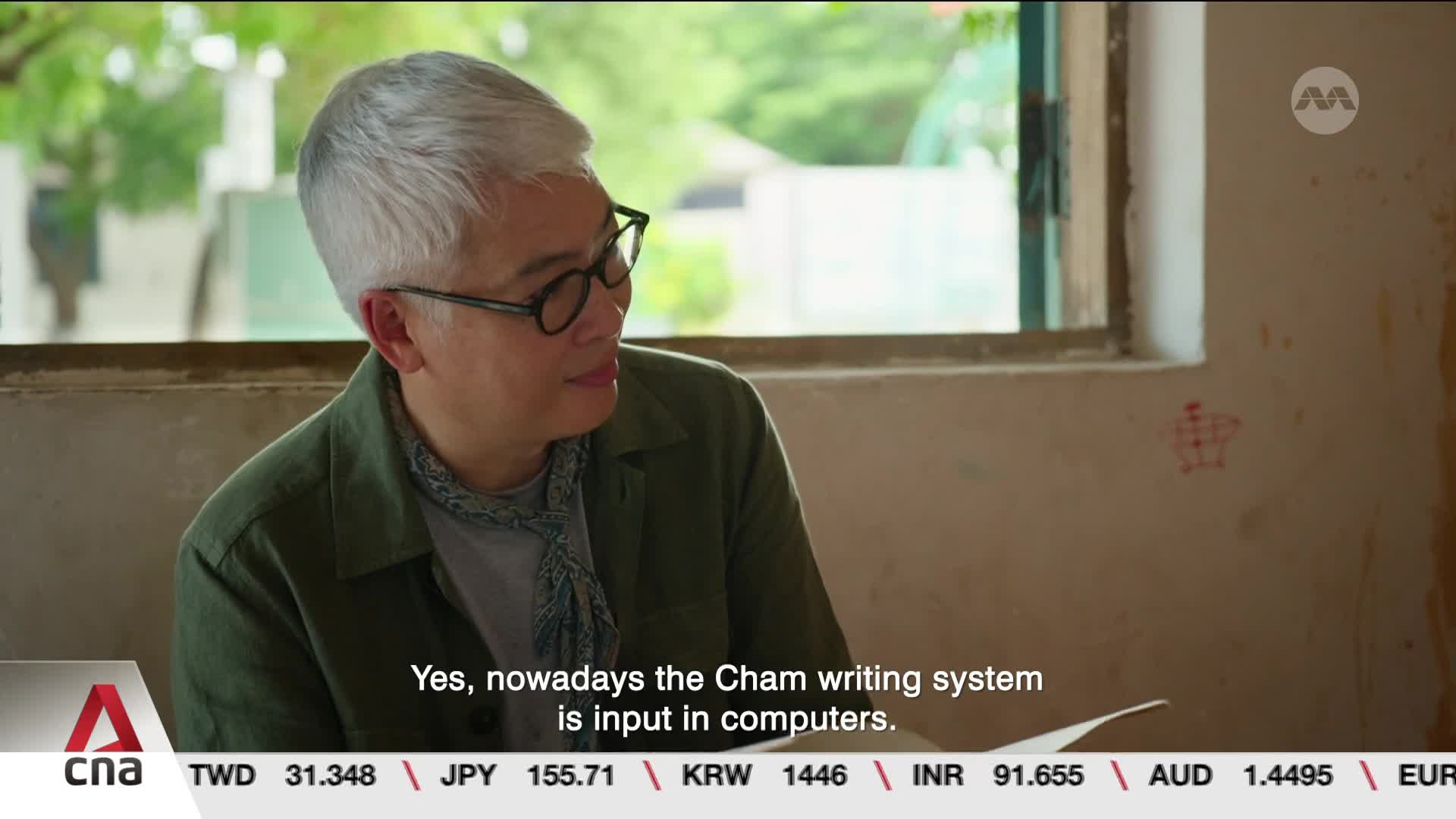 A man with grey hair and glasses speaks, his gaze directed slightly off-camera. Below him, a ticker displays currency exchange rates, with the CNA logo prominent. A man with grey hair and glasses speaks, his gaze directed slightly off-camera. Below him, a ticker displays currency exchange rates, with the CNA logo prominent.