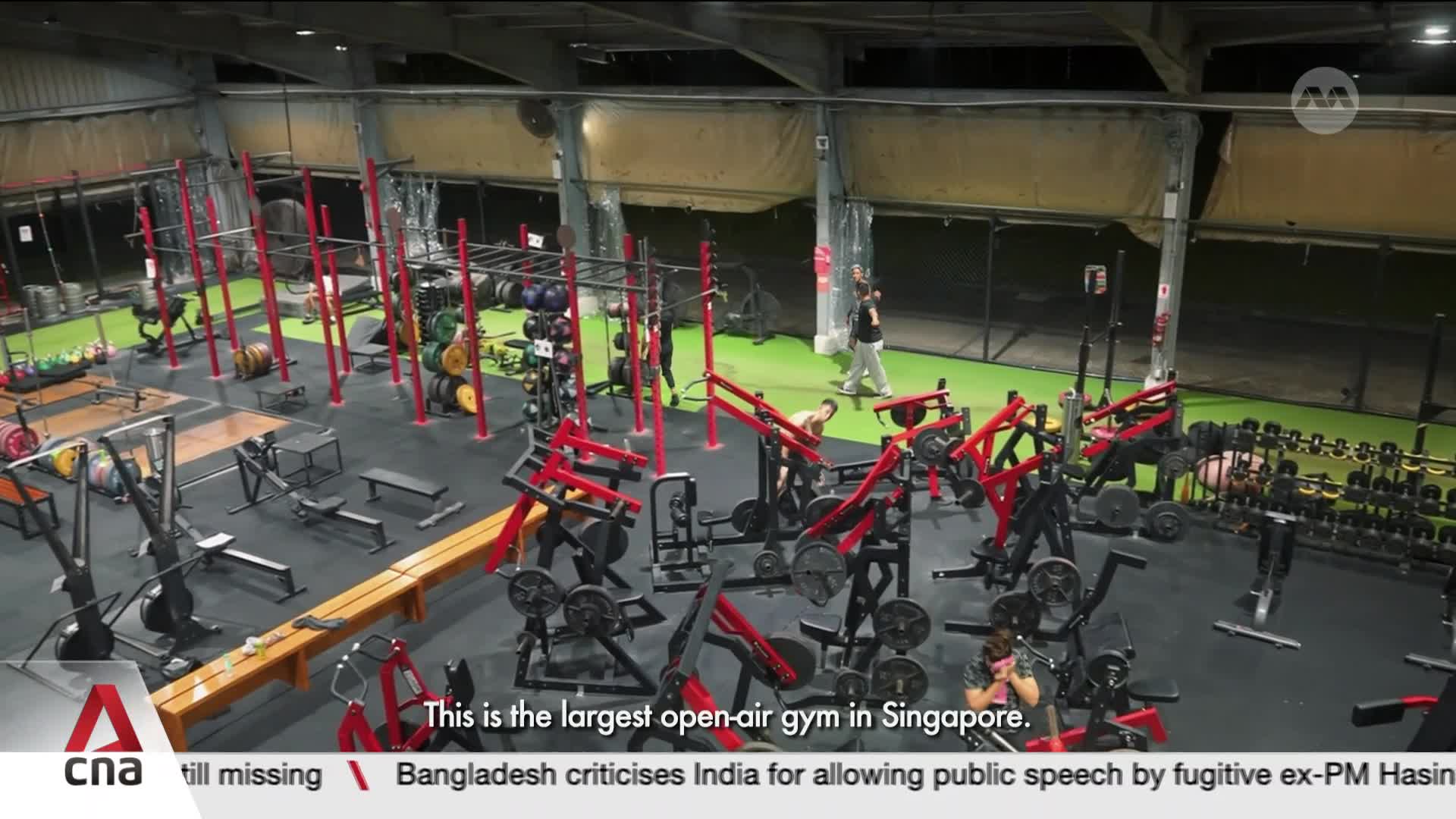 A man in a black shirt walks across the green floor, while another person is seated on a weight machine. This is the largest open-air gym in Singapore. A man in a black shirt walks across the green floor, while another person is seated on a weight machine. This is the largest open-air gym in Singapore.