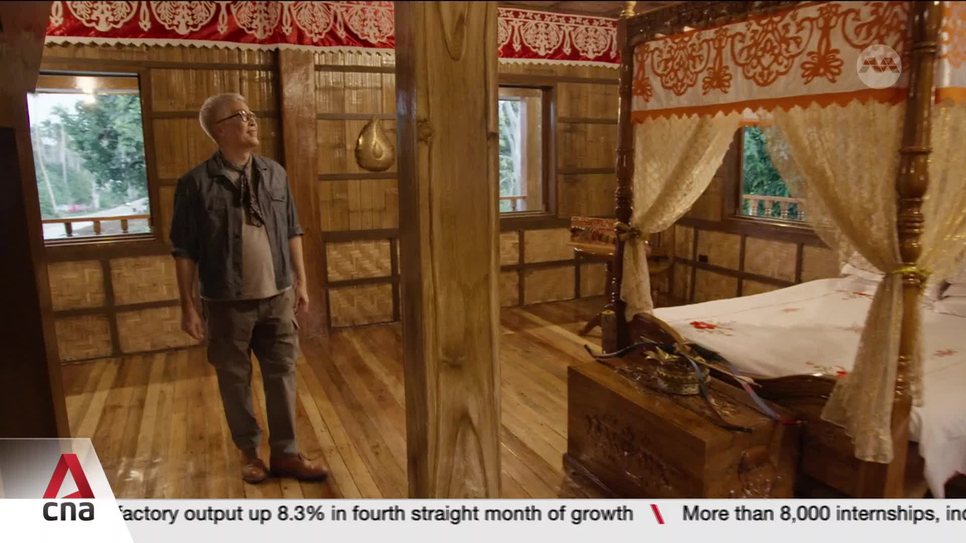 A man stands in a room with bamboo walls and a wooden floor, looking up. A large, ornate four-poster bed dominates the right side of the space. A man stands in a room with bamboo walls and a wooden floor, looking up. A large, ornate four-poster bed dominates the right side of the space.