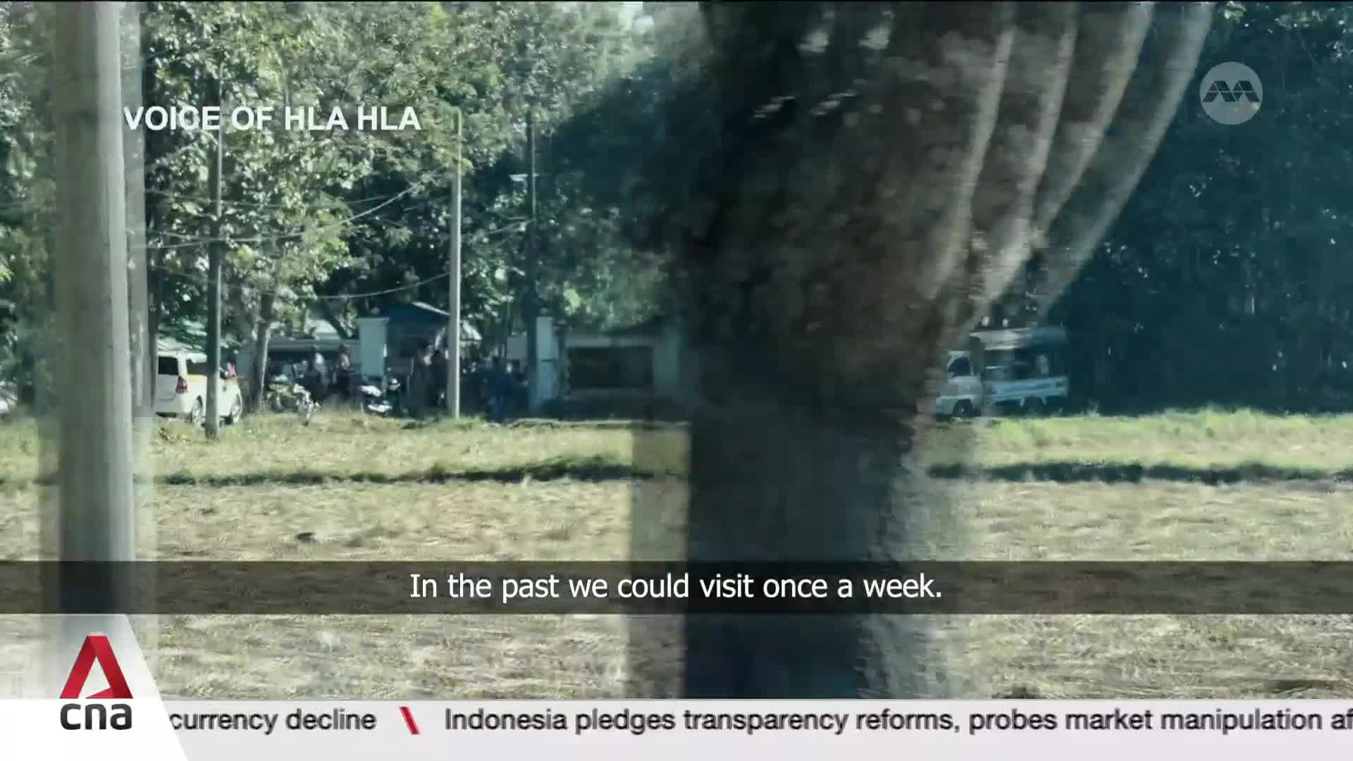 A white truck drives past a grassy field and some trees. A group of people are gathered near a few parked vehicles and buildings in the distance. A white truck drives past a grassy field and some trees. A group of people are gathered near a few parked vehicles and buildings in the distance.