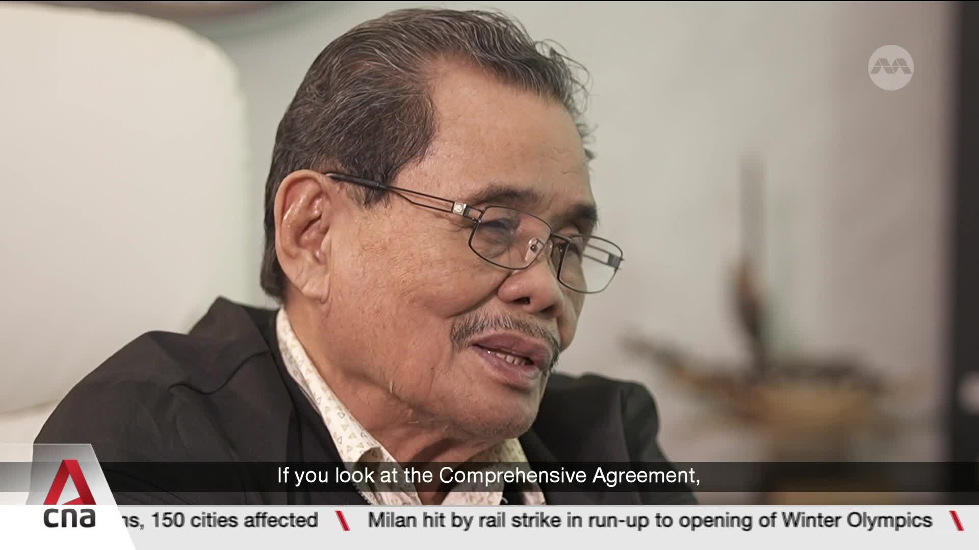 An older gentleman with glasses and a mustache speaks, his mouth slightly open. Below him, a news ticker scrolls, mentioning a "Comprehensive Agreement" and a rail strike in Milan. An older gentleman with glasses and a mustache speaks, his mouth slightly open. Below him, a news ticker scrolls, mentioning a "Comprehensive Agreement" and a rail strike in Milan.