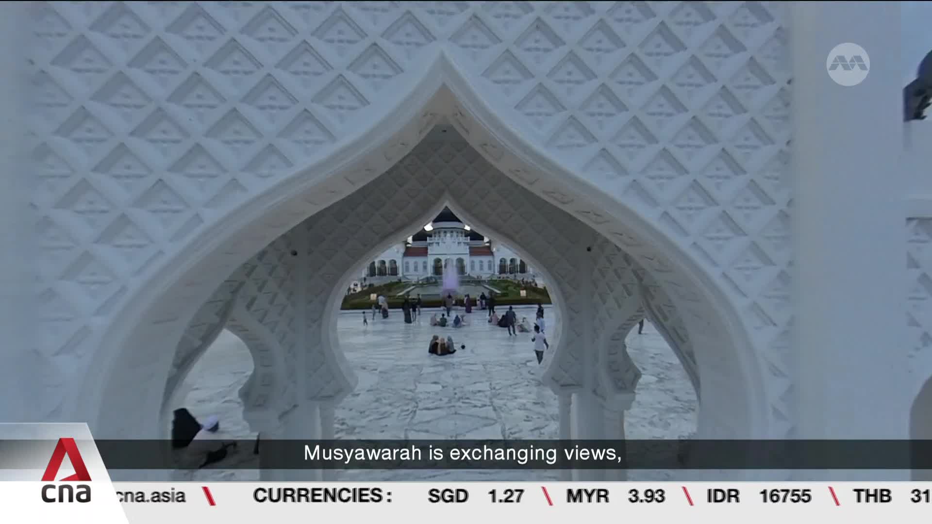 People are gathered in a wide, marble-paved courtyard before a grand white building. A fountain sprays water in the distance, and a few individuals stroll across the open space. People are gathered in a wide, marble-paved courtyard before a grand white building. A fountain sprays water in the distance, and a few individuals stroll across the open space.