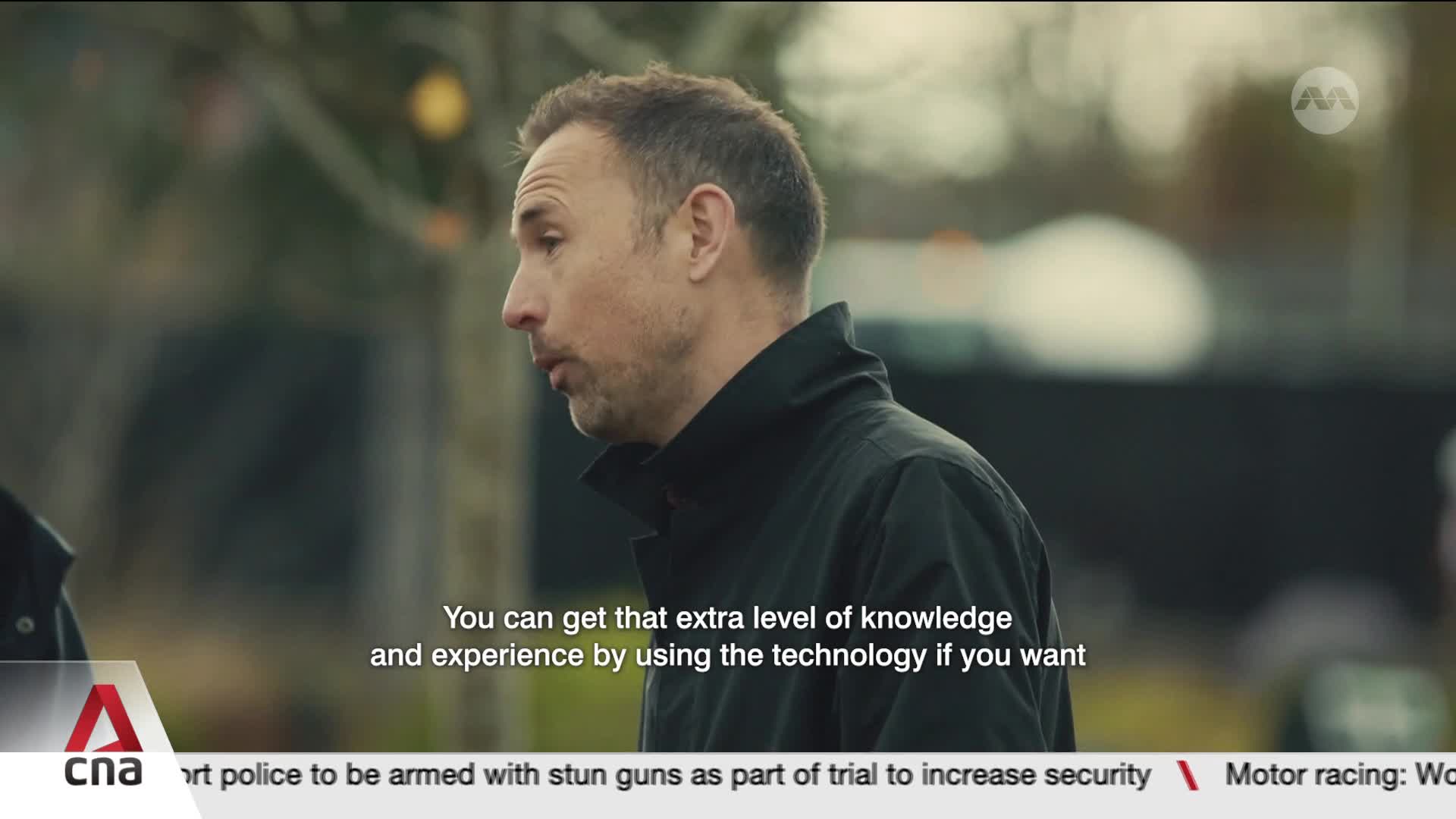 A man in a dark jacket speaks, his profile sharp against a blurred background. Below him, a news ticker from CNA International reports on Singaporean police trials for stun guns. A man in a dark jacket speaks, his profile sharp against a blurred background. Below him, a news ticker from CNA International reports on Singaporean police trials for stun guns.