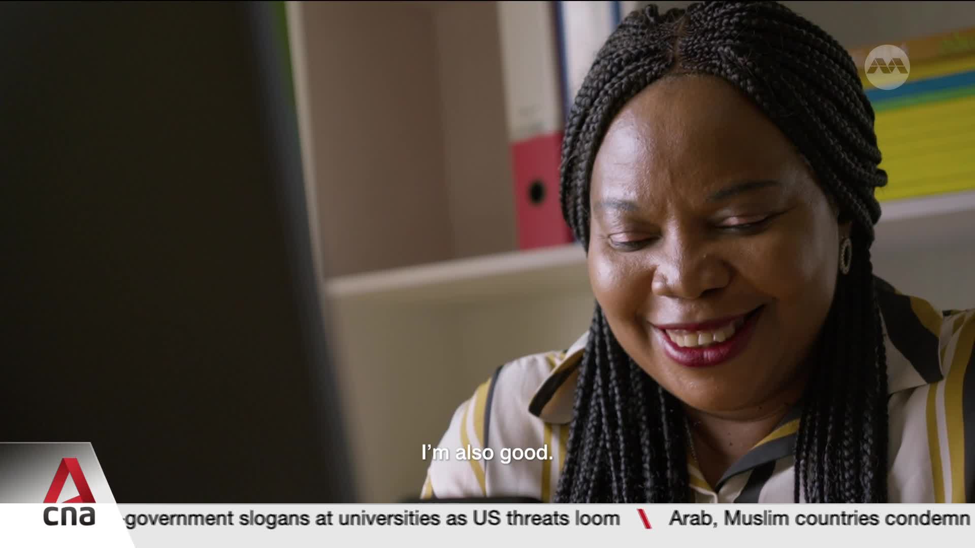 A woman with braided hair smiles as she looks down. She's wearing a striped shirt, and the CNA logo is visible in the corner. A woman with braided hair smiles as she looks down. She's wearing a striped shirt, and the CNA logo is visible in the corner.