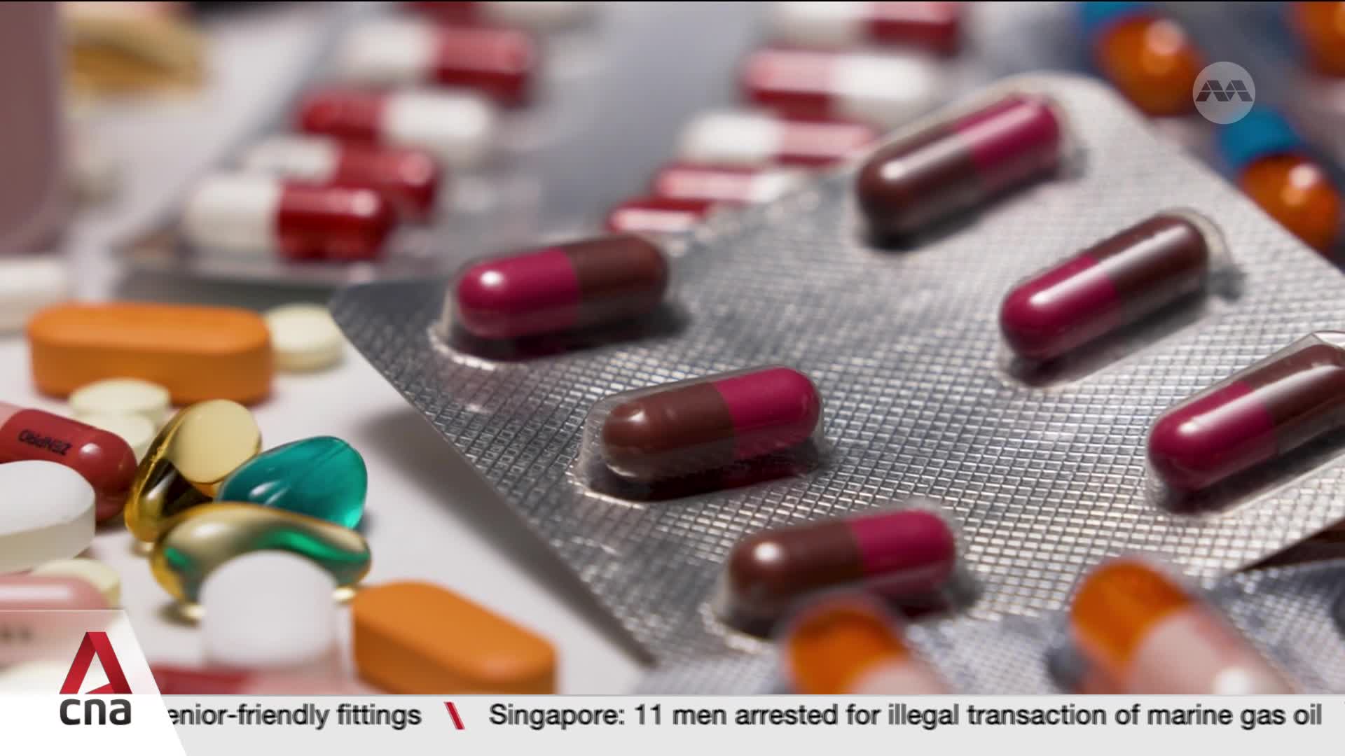 Rows of red and white capsules sit in blister packs, some scattered loose with oval orange tablets and colorful gel capsules. The CNA International logo appears in the corner, hinting at a report from Singapore. Rows of red and white capsules sit in blister packs, some scattered loose with oval orange tablets and colorful gel capsules. The CNA International logo appears in the corner, hinting at a report from Singapore.