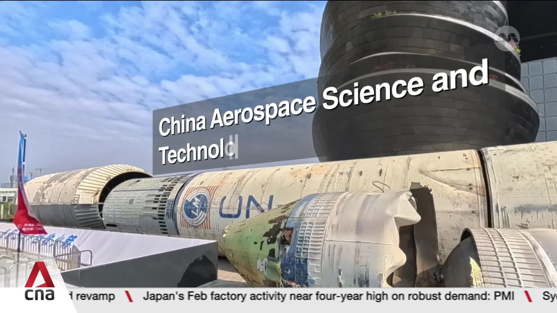 A colossal rocket, weathered and sectioned, lies horizontally before a modern, curved building. The text "China Aerospace Science and Technology" overlays the scene, hinting at an exhibition.