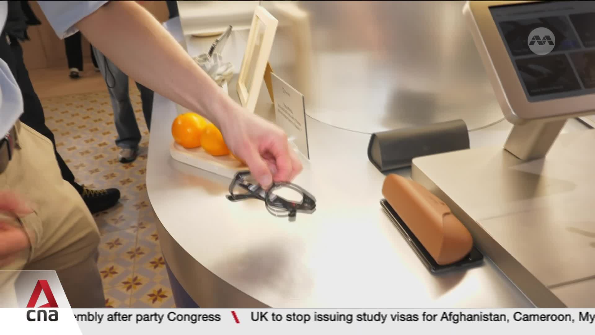 A hand reaches for a pair of glasses on a counter. Two bright orange fruits sit on a small wooden board nearby.