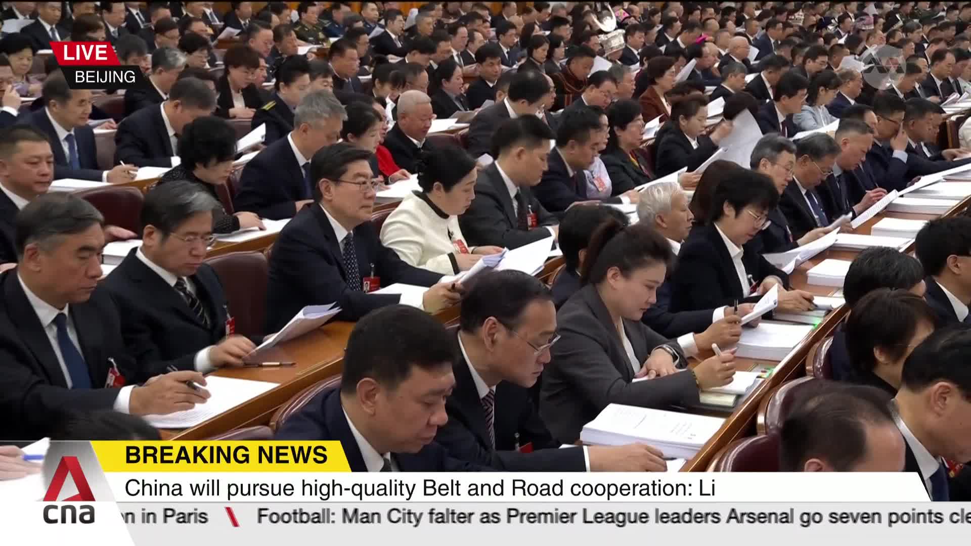 A large assembly of people in suits and formal attire are seated at long tables, many holding papers and pens. The news ticker at the bottom indicates a live broadcast from Beijing, with CNA reporting on China's pursuit of high-quality Belt and Road cooperation.