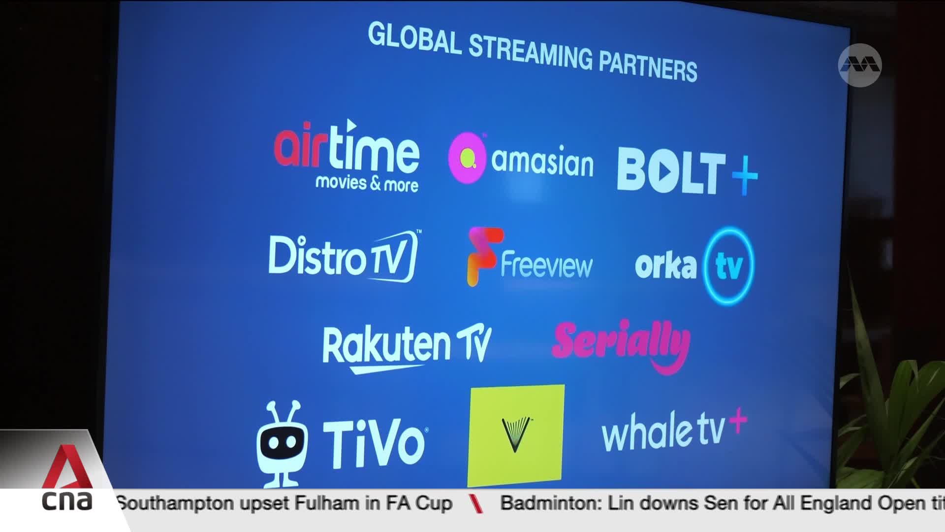 A screen displays a grid of logos for global streaming partners, including "airtime," "Distro TV," and "Rakuten TV." Below, the CNA logo anchors a ticker with news headlines.