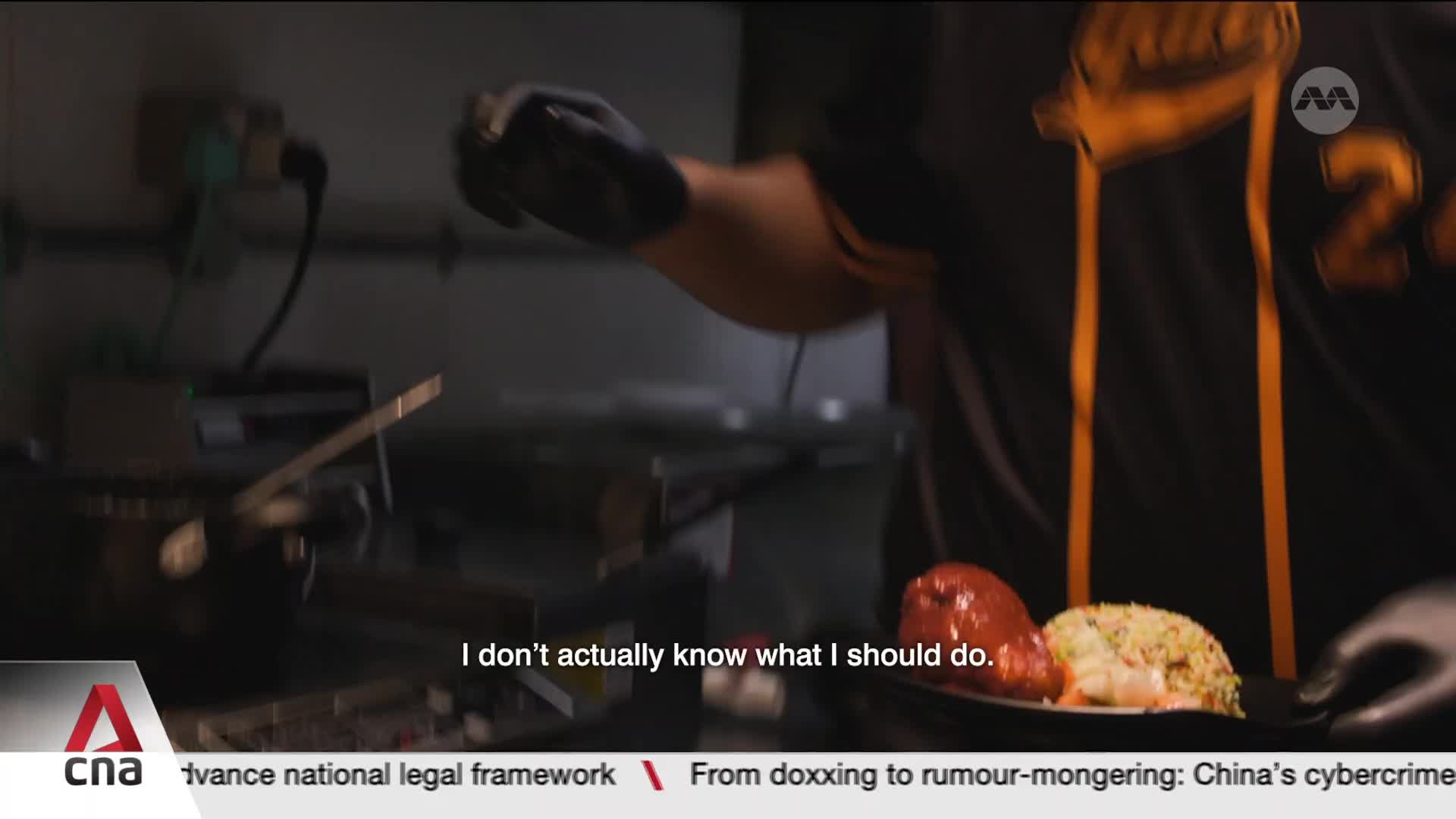A gloved hand places a plate with glistening red chicken and a mound of fried rice onto a counter. The person wearing the plate is dressed in a dark shirt with yellow trim, a common sight in Singapore's bustling food scene.