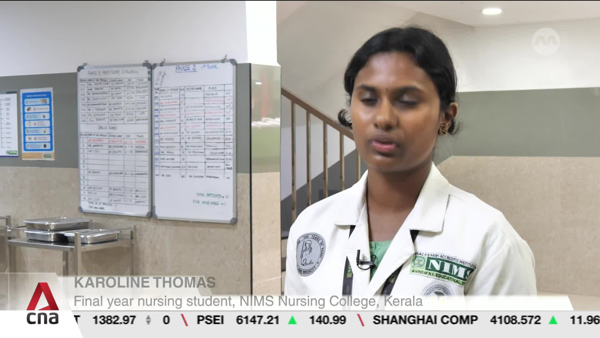 A young woman in a white nursing uniform speaks directly to the camera. Behind her, a whiteboard displays a grid of handwritten notes and charts.
