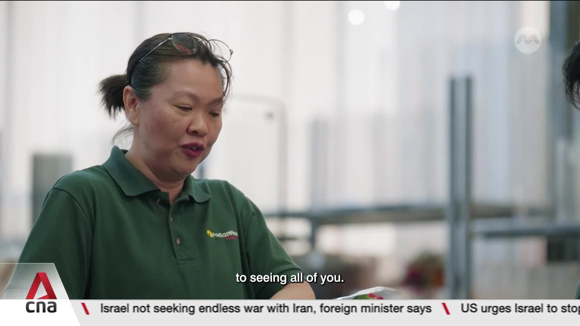 A woman in a green polo shirt speaks, her glasses perched on her head. The CNA logo and a news ticker are visible at the bottom of the frame.