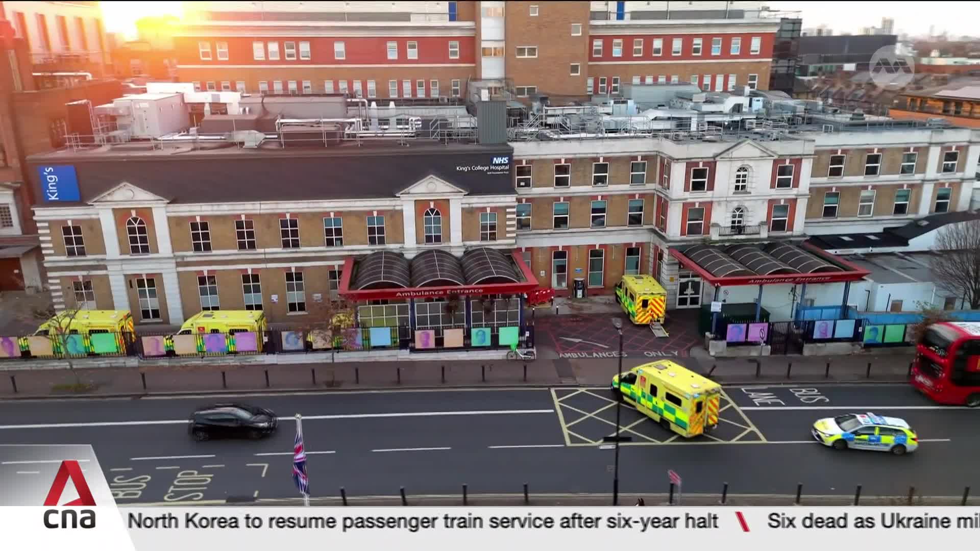 Ambulances are parked outside King's College Hospital. A police car and a red double-decker bus are on the road.