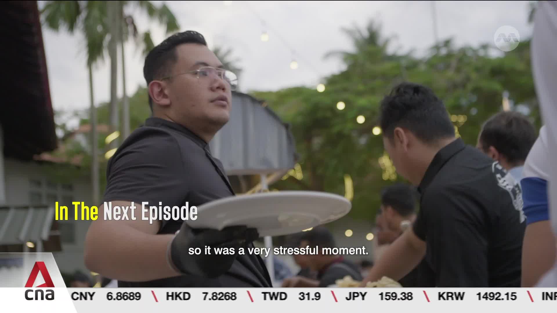 A man in a black shirt holds a white plate, looking off to the side. Others in black shirts are serving food behind him.
