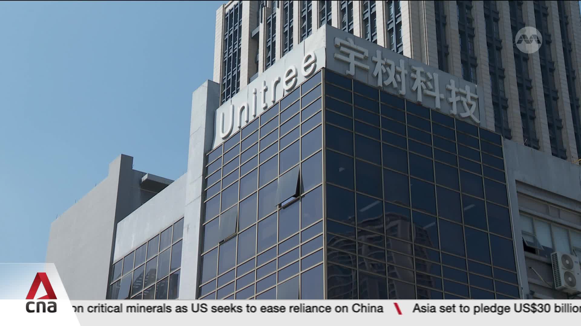 The sun glints off the mirrored windows of a modern office building, its facade bearing the name "Unitree" in large white letters. Below, a news ticker from CNA International scrolls by, mentioning critical minerals and Asia's pledge of US$30 billion.