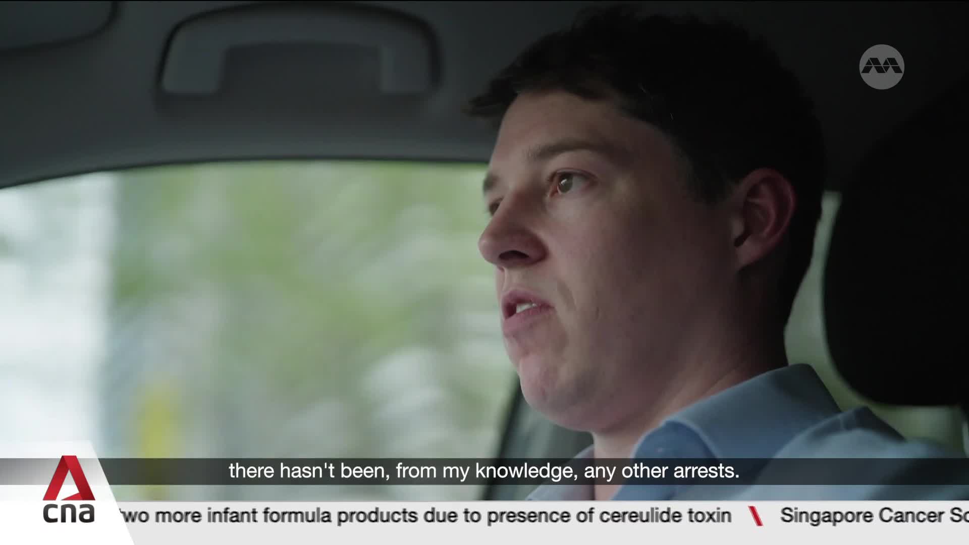 The man in the driver's seat is speaking, his gaze fixed forward. Outside the car window, the Singaporean scenery passes by, a green blur. The man in the driver's seat is speaking, his gaze fixed forward. Outside the car window, the Singaporean scenery passes by, a green blur.