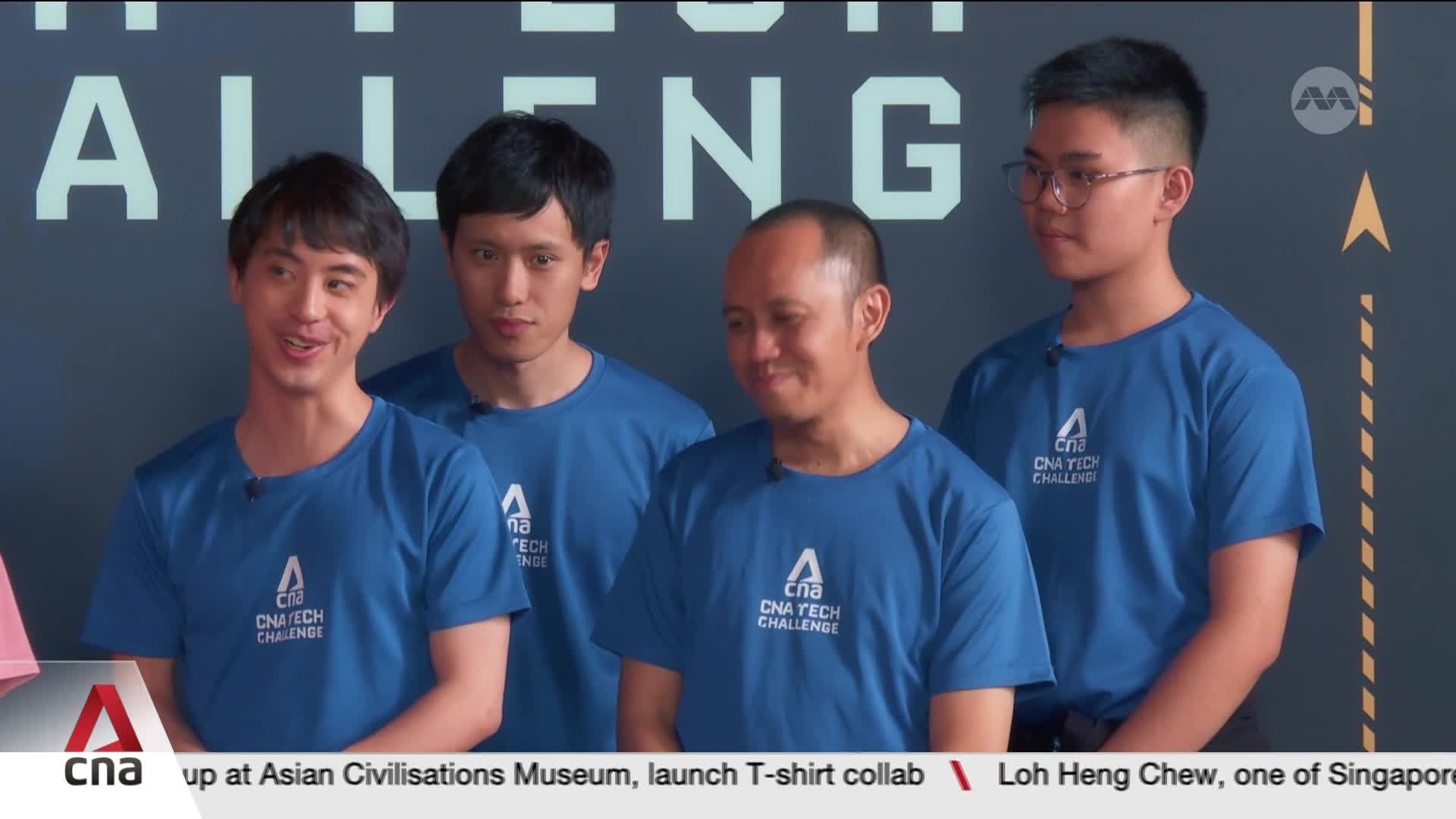 Four young men stand in bright blue t-shirts with "CNA Tech Challenge" printed on them. The backdrop behind them features large, light-colored lettering that reads "CHALLENGE."