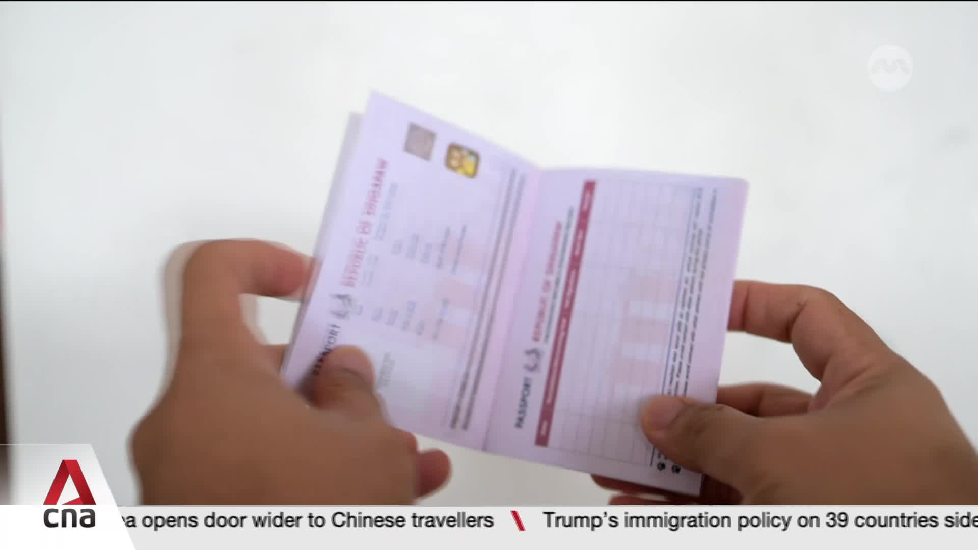 Fingers turn the pages of a Singapore passport. The document is held open, revealing printed text and a small emblem.