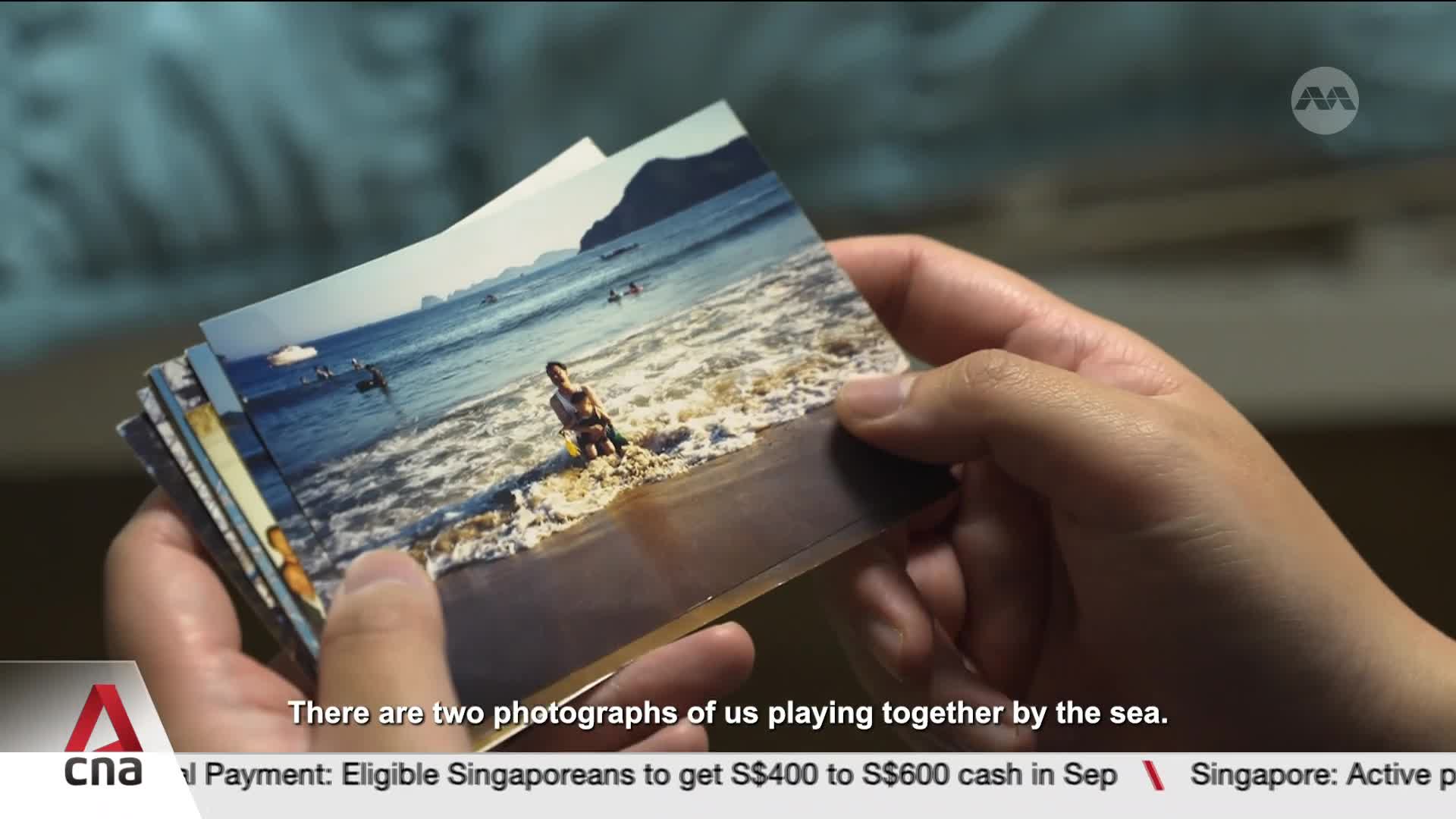 Fingers hold a stack of photographs, revealing a sun-drenched beach scene. Waves break gently on the shore where a figure sits, captured in a moment of seaside play.