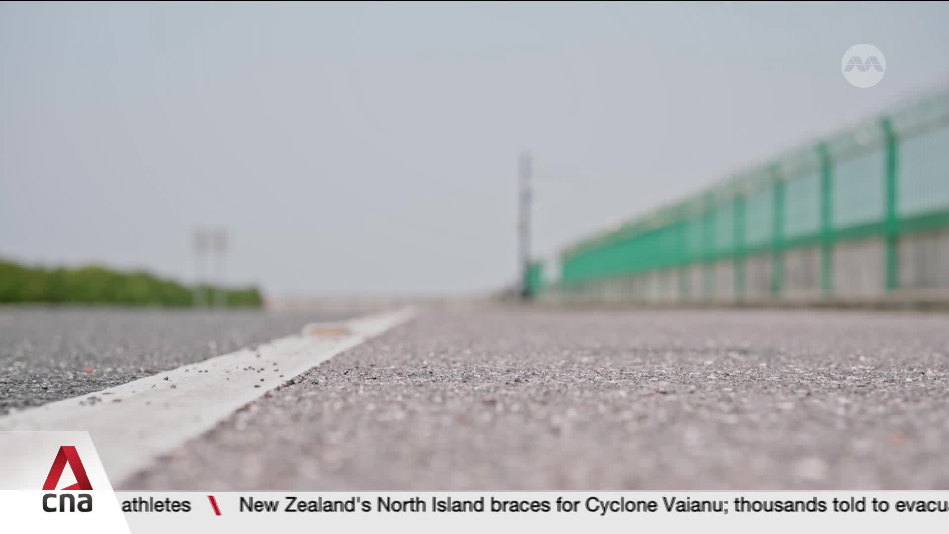 The asphalt stretches out, a white line marking its edge. A long, green barrier runs alongside the road, disappearing into the hazy distance.