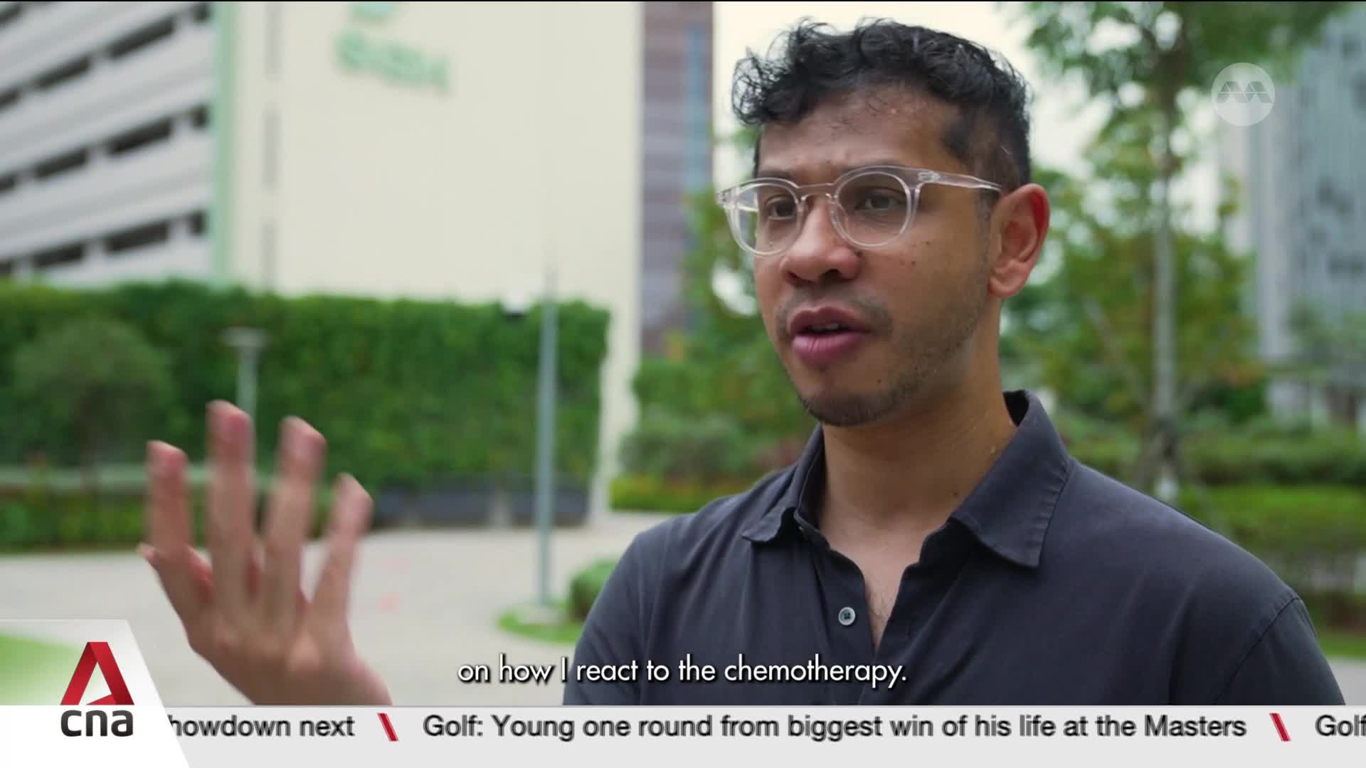 A man with glasses speaks, gesturing with his left hand. Behind him, a building and greenery are visible, with a CNA watermark in the corner.