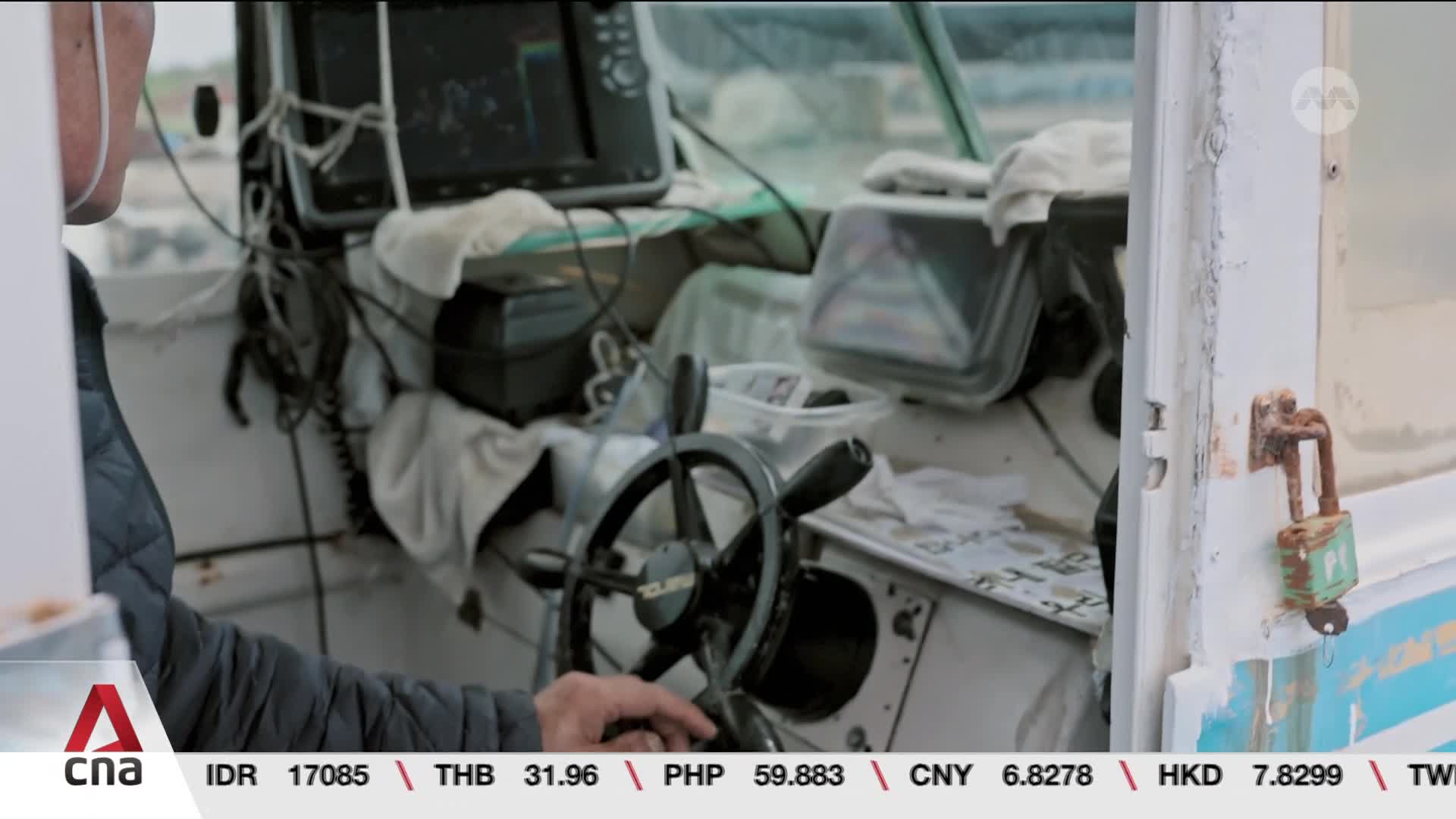 A hand grips the helm of a small vessel, the captain's face obscured by a mask. Wires snake across the console, leading to a navigation screen displaying what looks like sonar readings.