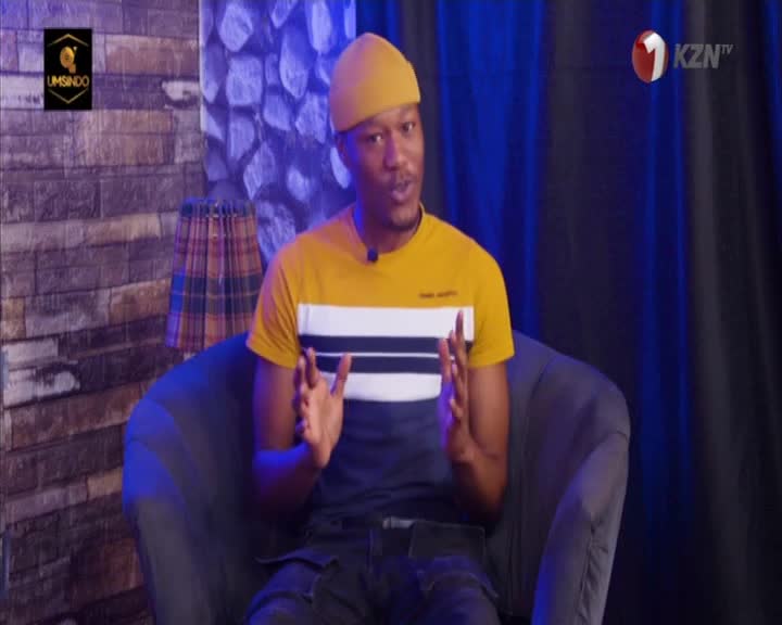 The man seated in the chair gestures with both hands, speaking to the camera. The 1KZN TV logo sits in the corner as he talks, likely on a show from South Africa.
